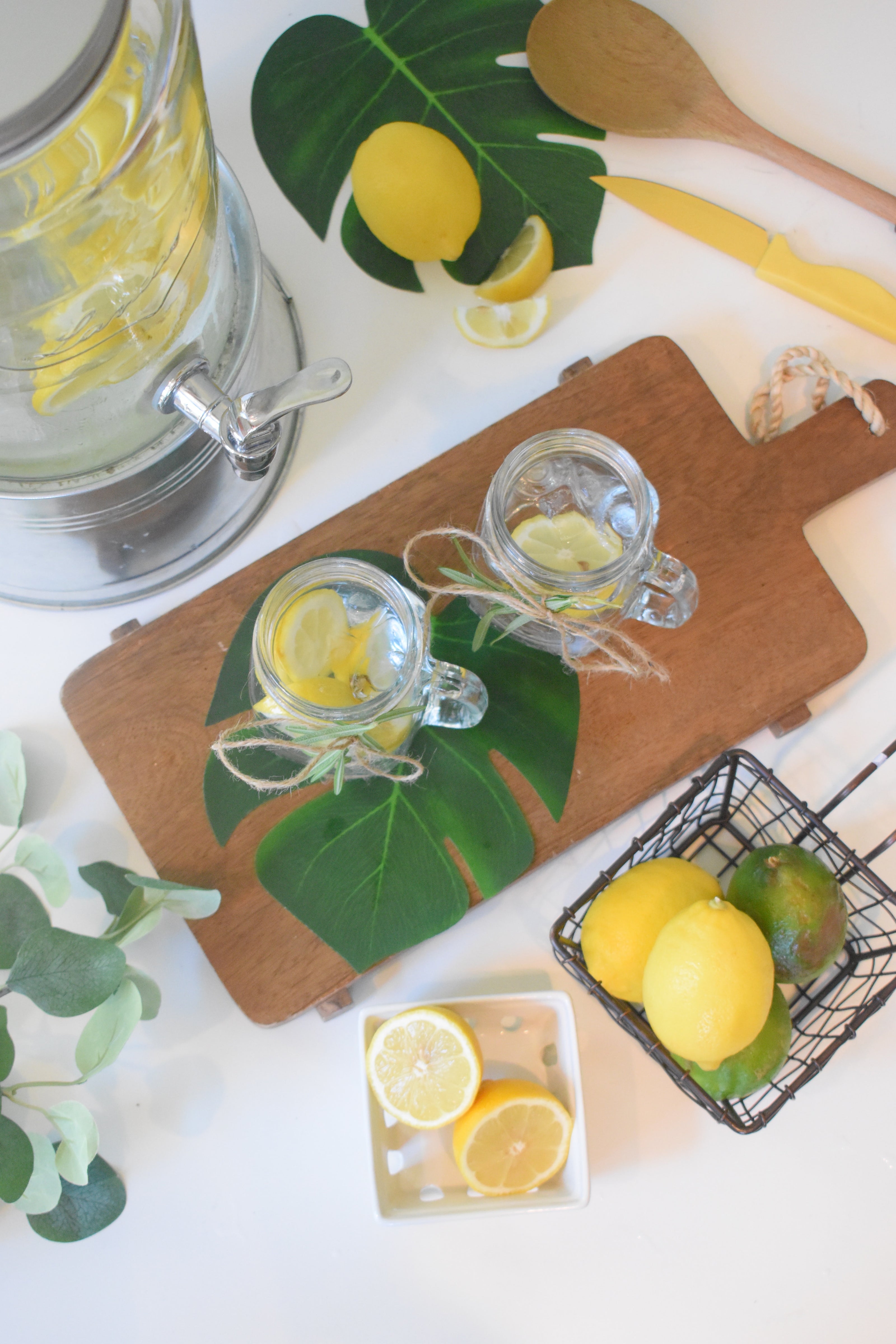 A kitchen scene featuring a water pitcher filled with lemon water, surrounded by sliced lemons and limes on a wooden cutting board.